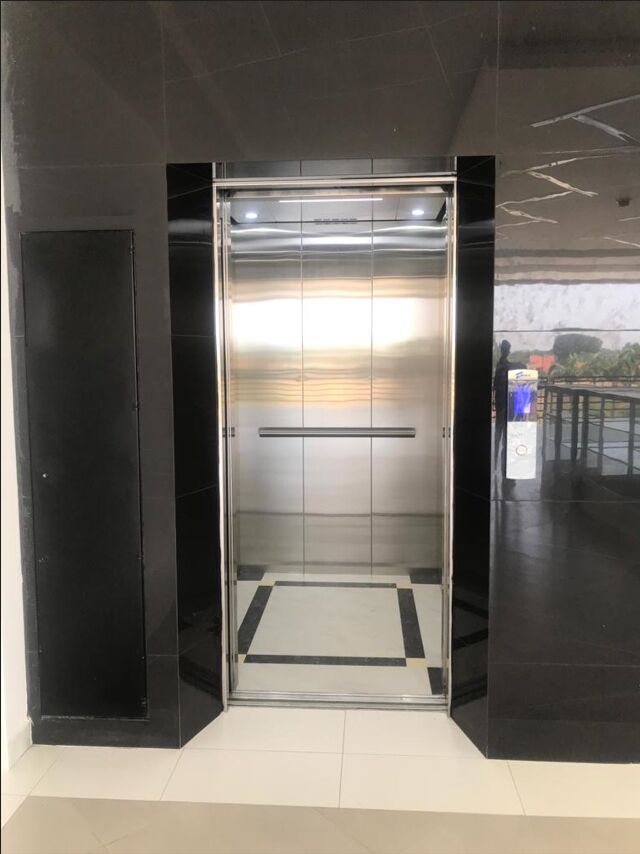 Ascensor con acabado en acero inoxidable instalado en un lobby de mármol negro